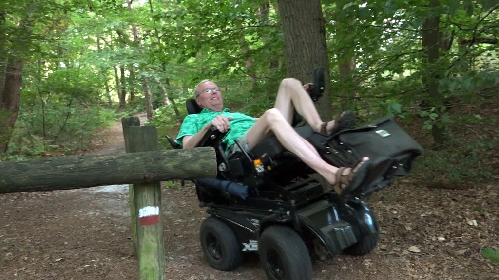 Een man in een elektrische rolstoel test of hij door een houten natuurpoort kan met zijn rolstoel